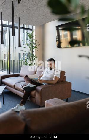 Porträt eines jungen erwachsenen Reisenden, der eine Zeitung auf Sofa für Fenster liest Stockfoto
