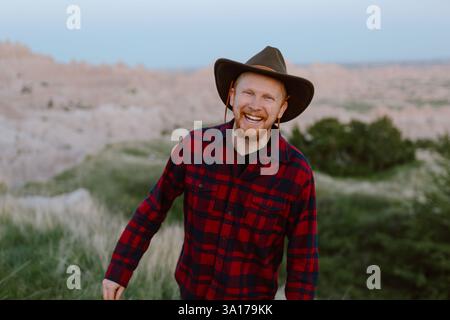 Lächelnder Reisender in Cowboyhut genießt die Badlands bei Sonnenuntergang. Stockfoto