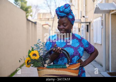 Junge Frau, die Sonnenblumen und Eukalyptus in einem Korb trägt Stockfoto