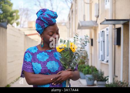 Frau riecht Sonnenblumen und Eukalyptusstrauß auf der Straße Stockfoto