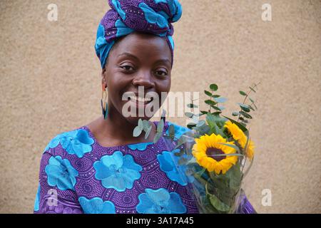 Lächelnde afrikanerin mit Sonnenblumen und Eukalyptusstrauß Stockfoto