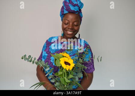 Lächelnde Afrikanerin mit Sonnenblumen und Eukalyptusstrauß Stockfoto
