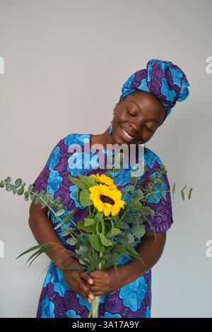 Lächelnde Afrikanerin mit Sonnenblumen und Eukalyptusstrauß Stockfoto