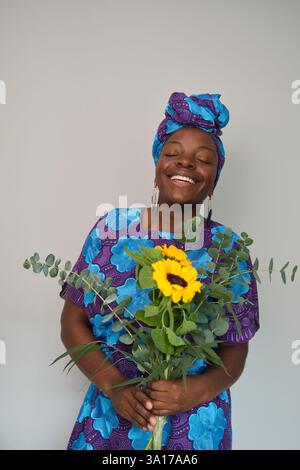 Afrikanische Frau lacht und hält Sonnenblumen und Eukalyptusstrauß Stockfoto