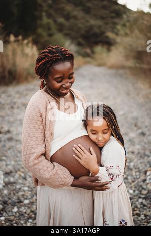 Lächelndes schwarzes Race Girl umarmt schwarzen schwangeren Mutterbauch Stockfoto