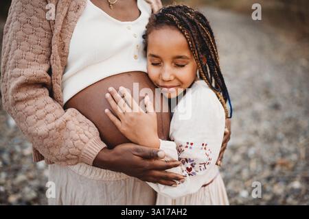 Lächelndes schwarzes Race Girl umarmt schwarzen schwangeren Mutterbauch Stockfoto