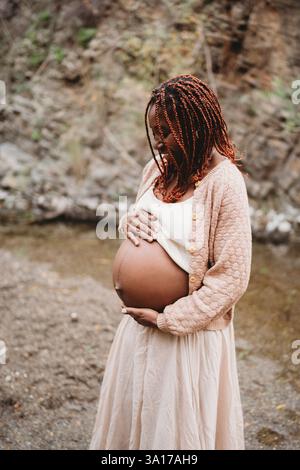 Schwarz erwartet schwangere Frau draußen am Fluss Stockfoto