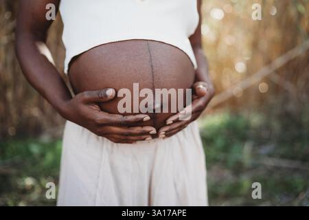 Glückliche schwarze Frau lächelt schwanger und zeigt Bauchfelder Sommer Stockfoto