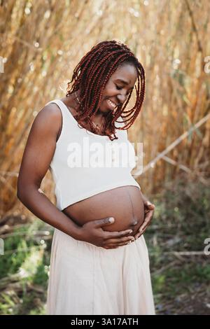 Glückliche schwarze Frau lächelt schwanger und zeigt Bauchfelder Sommer Stockfoto