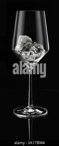 Wine glass filled with ice cube cubes in front of a black background, studio shot Stockfoto