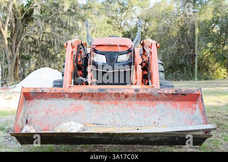 Orangefarbener Frontlader-Traktor auf einer Baustelle mit Schmutz und Stockfoto