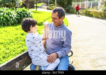 Großvater und Enkel genießen eine gute gemeinsame Zeit, spielen und lachen auf einer Parkbank an einem sonnigen Tag Stockfoto