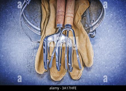 Metalleimer Handrechen Kelle Gabel Leder Schutzhandschuhe auf metallischem Hintergrund Gartenkonzept Stockfoto