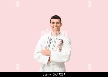 Porträt eines hübschen jungen Mannes im Bademantel mit Zeitung auf rosa Hintergrund Stockfoto