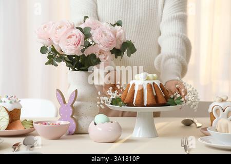 Frau, die ein Tablett mit Osterkuchen auf dem Tisch hält, um die Osterfeier im Zimmer zu feiern. Nahaufnahme Stockfoto
