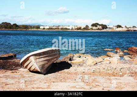 Verlassenes weißes Boot an der Küste vor blauem Wasser unter der sengenden Sonne liegt ein altes Boot auf den Felsen in der Nähe des Meeres Stockfoto