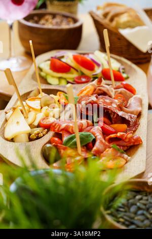 Eine rustikale Wurstplatte mit einer Auswahl an Wurstwaren, Käse, frischem Salat mit Tomaten und Gurken und einem Korb mit Brotscheiben. Die Stockfoto