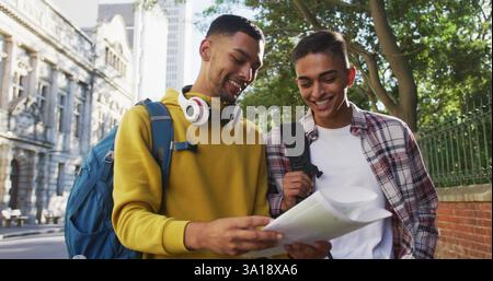 Zwei glückliche männliche Freunde, die auf der Straße spazieren gehen und eine Karte benutzen Stockfoto