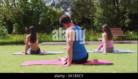 Rückansicht der verschiedenen Gruppen, die Yoga üben, sitzen auf Matten im Park Stockfoto