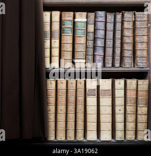 Bücher mit Lederbindung (Werke von Gregory Nazianzus, Ambrose, Dionysius, Jerome und Augustine) in Regalen in der Bibliothek Wren, Trinity College, Universität Stockfoto