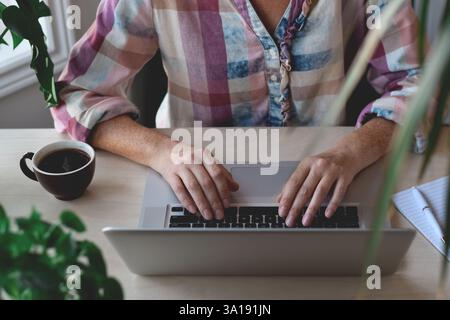 Die Hände einer Frau von oben, die am Schreibtisch sitzt und auf einem Laptop schreibt Stockfoto