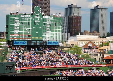 Die Fans gehen auf das Baseballteam der Chicago Cubs, während sie unter der historischen, manuell betriebenen Anzeigetafel im Wrigley Field sitzen Stockfoto