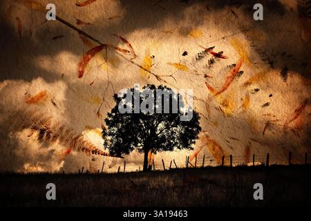 Ein hoher, einsamer Baum steht auf einem grasbewachsenen Hügel, der sich vor einem stimmungsvollen Himmel voller Wolken und herabfallender Herbstblätter befindet. Stockfoto