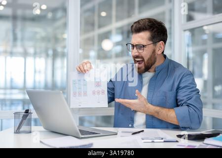 Wütender Mann auf Online-Meeting-Konferenz. Geschäftsmann, der Laptop für Videoanrufe benutzt, Einkommen vor der Kamera zeigt, unzufrieden schreien. Finanzanalyst im Büro. Stockfoto