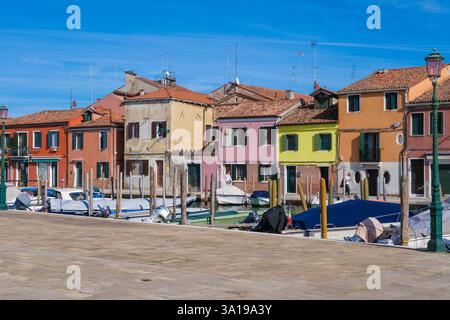 Venedig, Italien - 12. Oktober 2024: Eine Reihe von bunten Häusern mit lebhaften Fassaden säumt einen ruhigen Kanal in Murano, mit kleinen Booten, die entlang des Wassers vertäut sind Stockfoto