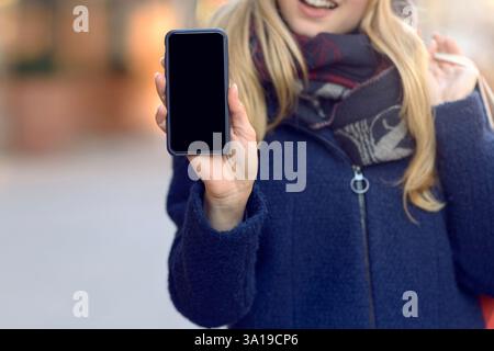 Eine hübsche junge Frau, die ihr Handy mit einem leeren Display hochhält Stockfoto