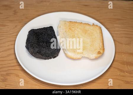 Geröstetes und vollständig verbranntes Brötchen, das auf einem weißen Teller sitzt Stockfoto