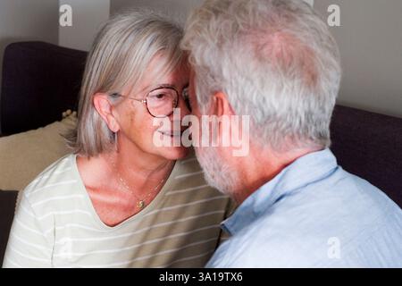 Herzerwärmende Szene eines reifen Paares, eines liebevollen Mannes und einer liebevollen Frau, die zu Hause auf dem Sofa kuschelt. Die Großeltern teilen süße Momente der Zuneigung, flirten und plaudern gemütlich drinnen und genießen ihre goldenen Jahre miteinander Stockfoto