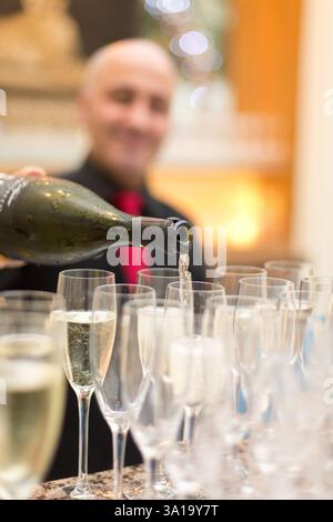 Champagner wird in einem Londoner Hotel in Gläser gegossen. Ein Kellner gießt für eine Gruppe. Stockfoto