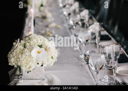 Der wunderschön angeordnete Tisch mit weißen Blumenmustern und glitzernden Gläsern sorgt für ein elegantes Treffen. Stockfoto