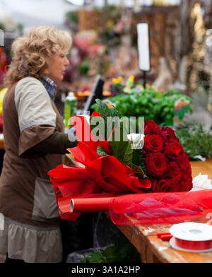 Blumengeschäft mit professionellen Kleidung in einer Baumschule. Vorbereitung eines Strauß roter Rosen. Stockfoto