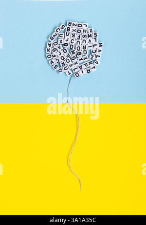 Ballon aus Buchstaben auf gelbem und blauem Hintergrund. Konzeptuelles Bild von Literatur, Sprache und Meinungsfreiheit. Stockfoto