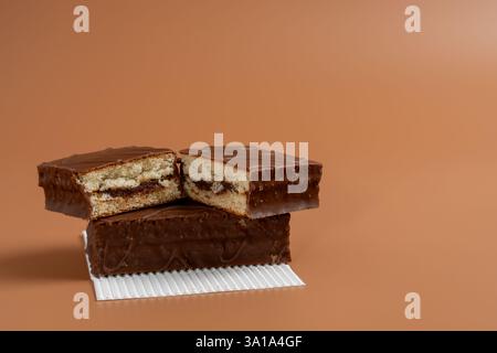 Ein köstlicher Schokoladenkuchen wird in zwei Hälften geschnitten und auf weißem Papier vor braunem Hintergrund gelegt. Der Kuchen wird in zwei Hälften geschnitten und auf ein weiteres C gelegt Stockfoto