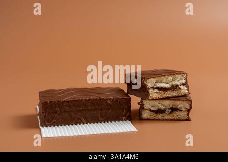 Ein Schokoladenkuchen liegt auf weißem Papier. Ein weiterer Kuchen wird in zwei Hälften geschnitten. Beide Kuchen sind auf braunem Hintergrund. Stockfoto