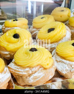 Aus nächster Nähe sehen Sie köstliches Zeppole, klassisches italienisches Gebäck gefüllt mit Vanillepudding und garniert mit einer dunklen Kirsche Stockfoto