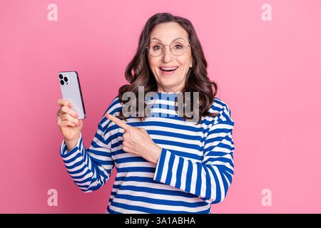Porträt einer energiegeladenen Seniorin, die ein Smartphone zeigt und selbstbewusst lächelt Stockfoto