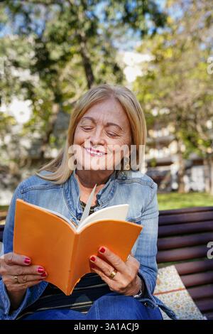 Reife Frau liest draußen im Park ein Buch Stockfoto