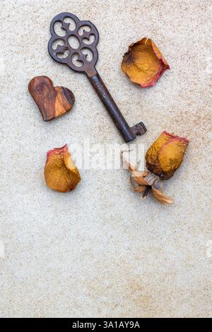 Alter Schlüssel mit dekorativem Herz und verwelkter Rose, Stillleben Stockfoto