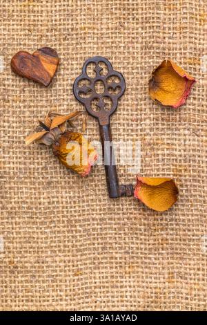 Alter Schlüssel mit dekorativem Herz und verwelkter Rose, Stillleben Stockfoto