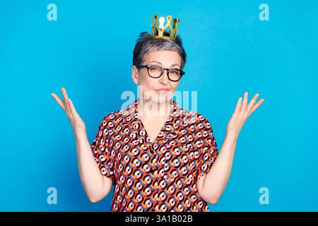 Porträt einer geblümten reiferen Frau mit Brille und spielerischer Geste vor einem leuchtenden blauen Hintergrund Stockfoto