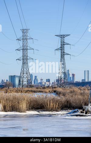 Zwei hochaufragende Kraftübertragungstürme dominieren die Skyline, mit gefrorenem Wasser und Marschland im Vordergrund. Die Skyline von Manhattan erscheint im d Stockfoto