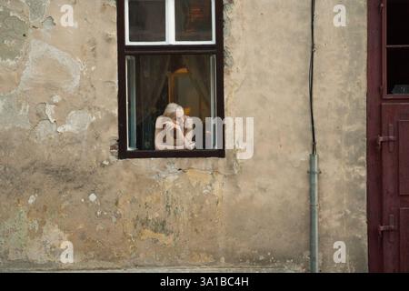 Eine ältere Frau schaut aus einem Fenster eines verwitterten Gebäudes in der Altstadt von Sibiu, Rumänien Stockfoto