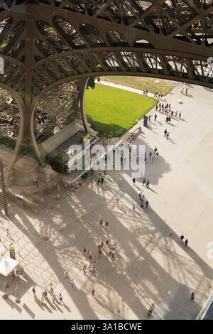 Touristen am Fuße des Eiffelturms in Paris, Frankreich, genießen das Gelände. Die Leute gehen, sitzen und stehen in der Warteschlange. Stockfoto