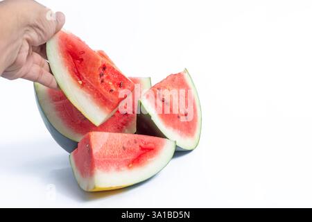 Ein Nahbild mit leuchtenden roten Wassermelonenschnitten auf weißem Hintergrund, das eine Hand zeigt, die eine aufnimmt. Stockfoto