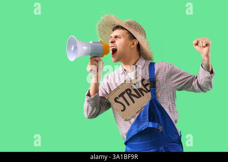 Protestierender männlicher Bauer mit einem Plakat, das in Megaphon auf grünem Hintergrund schreit. Schlagkonzept Stockfoto