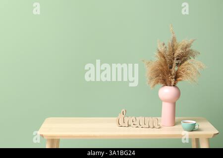 Hölzerner Couchtisch mit einer Tasse Tee, Vase mit Pampasgras und WORTTRAUM in der Nähe der grünen Wand im Zimmer Stockfoto